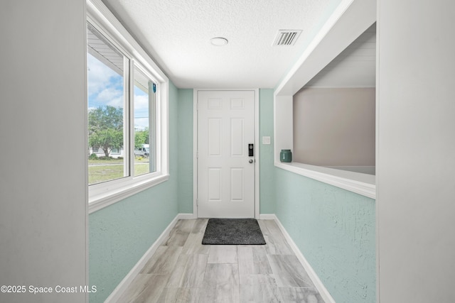 doorway with a textured ceiling, baseboards, and wood finished floors