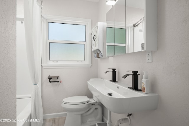 bathroom featuring toilet, a textured wall, a sink, and baseboards