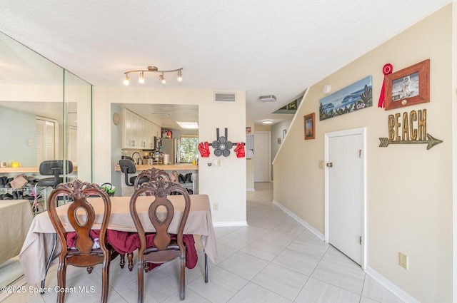 dining space with light tile patterned flooring, a textured ceiling, and baseboards