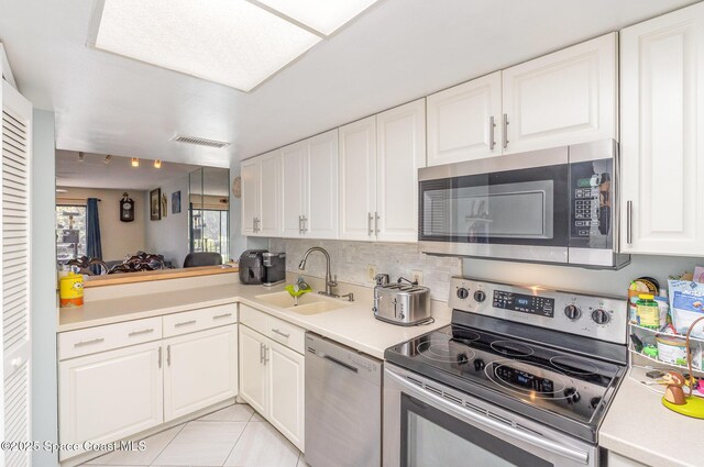 kitchen featuring stainless steel appliances, a sink, white cabinets, light countertops, and decorative backsplash