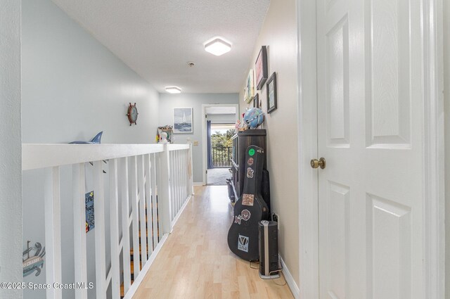 hall with light wood finished floors, a textured ceiling, and baseboards