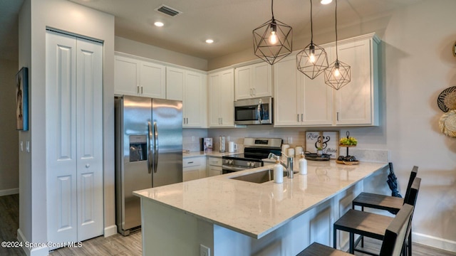 1272 Miraflores Trl NW, Palm Bay, FL 32907 - kitchen with stainless steel appliances, a peninsula, light wood-type flooring, white cabinetry, and light stone counters
