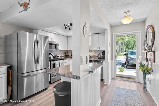 261 Cape Shores Cir Unit 18-E, Cape Canaveral, FL 32920 - kitchen with appliances with stainless steel finishes, a textured ceiling, tasteful backsplash, white cabinets, and light wood-style flooring