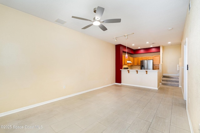 unfurnished living room featuring rail lighting, ceiling fan, and stairway