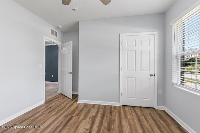 unfurnished bedroom featuring wood finished floors, baseboards, arched walkways, and ceiling fan