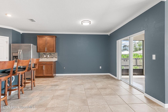 kitchen with crown molding, brown cabinetry, backsplash, baseboards, and light countertops