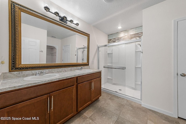 bathroom featuring a shower stall, double vanity, a textured ceiling, and baseboards