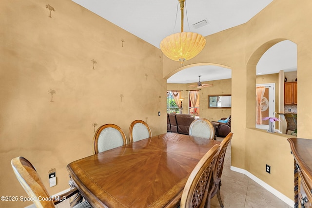 dining space with a ceiling fan, arched walkways, light tile patterned floors, and baseboards