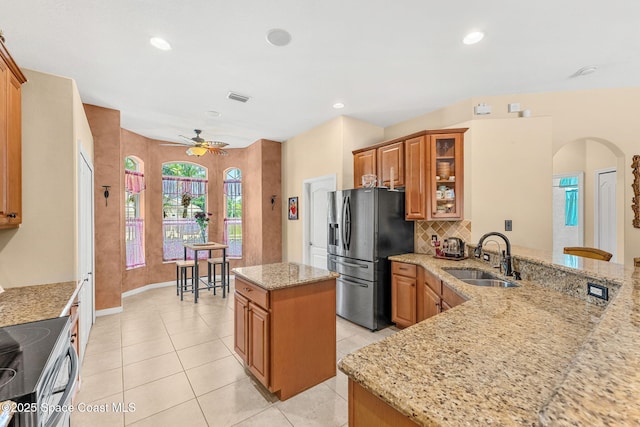 kitchen with a sink, stainless steel appliances, arched walkways, brown cabinets, and a ceiling fan