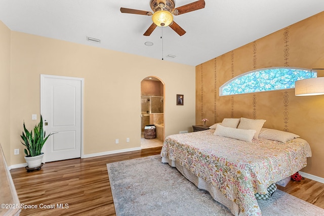 bedroom with arched walkways, wood finished floors, baseboards, connected bathroom, and ceiling fan