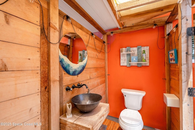 303 Winslow Cir, Cocoa Beach, FL 32931 - half bathroom featuring a sink, toilet, beam ceiling, wooden walls, and wood finished floors