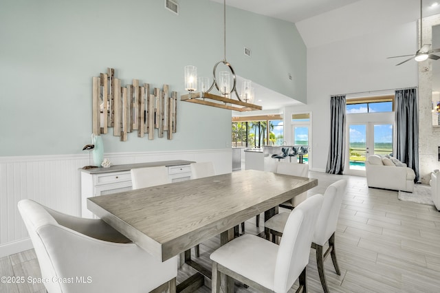 4070 S Tropical Trl, Merritt Island, FL 32952 - dining room featuring high vaulted ceiling, ceiling fan, a chandelier, a wainscoted wall, and healthy amount of natural light