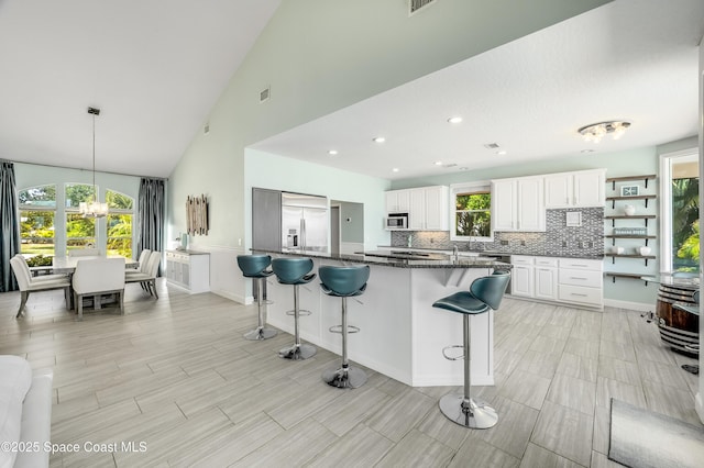 4070 S Tropical Trl, Merritt Island, FL 32952 - kitchen with stainless steel appliances, a breakfast bar, backsplash, white cabinetry, and high vaulted ceiling