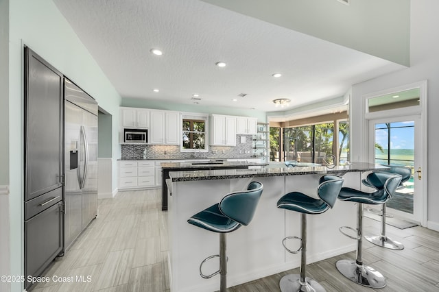 4070 S Tropical Trl, Merritt Island, FL 32952 - kitchen with built in appliances, a breakfast bar, white cabinetry, dark stone counters, and decorative backsplash
