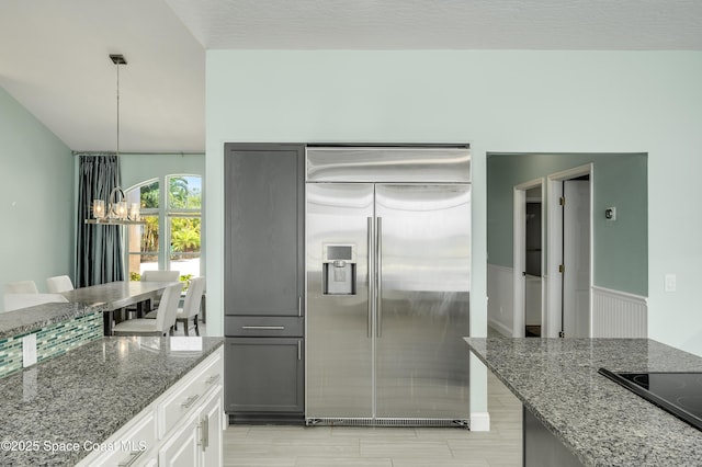 4070 S Tropical Trl, Merritt Island, FL 32952 - kitchen featuring stainless steel built in refrigerator, black electric cooktop, dark stone counters, a chandelier, and pendant lighting