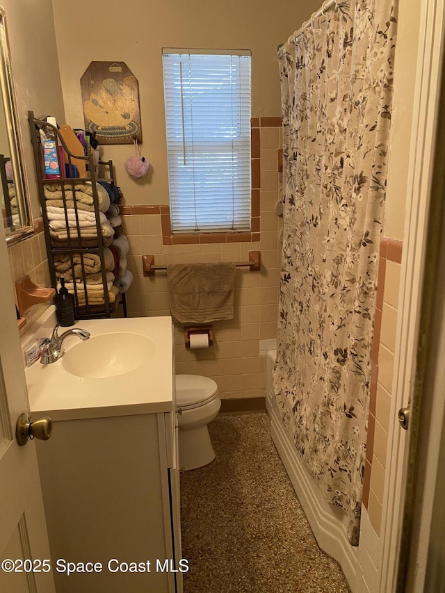 bathroom featuring tile walls, wainscoting, vanity, toilet, and shower / tub combo with curtain