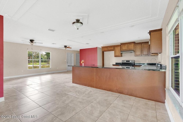kitchen with stainless steel range with electric stovetop, a sink, a ceiling fan, brown cabinets, and dark countertops