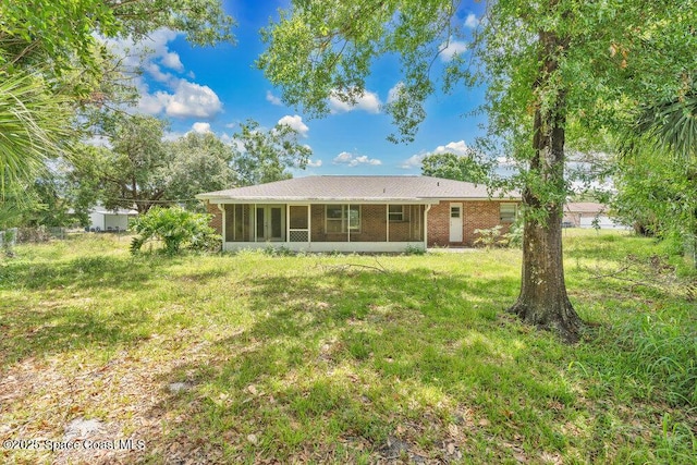 rear view of property with a sunroom, a lawn, and brick siding
