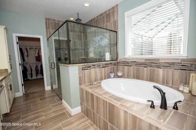 4407 Preservation Cir, Melbourne, FL 32934 - bathroom featuring a garden tub, a stall shower, a spacious closet, wood finish floors, and a textured ceiling