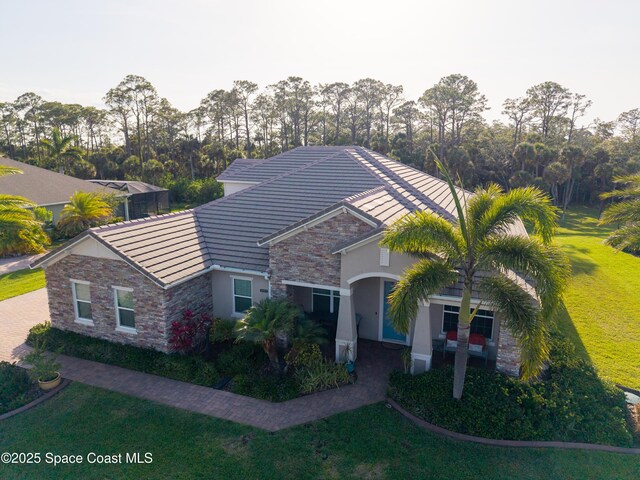 4407 Preservation Cir, Melbourne, FL 32934 - view of front of property featuring stone siding, a tile roof, a front lawn, stucco siding, and view of wooded area