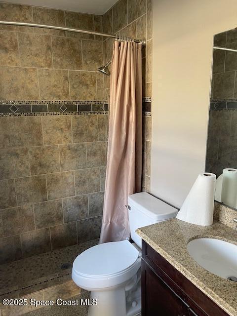 bathroom with tiled shower, vanity, and toilet