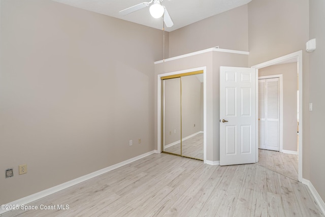 343 N Tropical Trl Unit 404, Merritt Island, FL 32953 - unfurnished bedroom with light wood-type flooring, baseboards, a closet, a towering ceiling, and ceiling fan