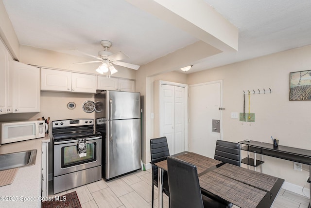 kitchen with stainless steel appliances, a ceiling fan, light countertops, a sink, and white cabinetry