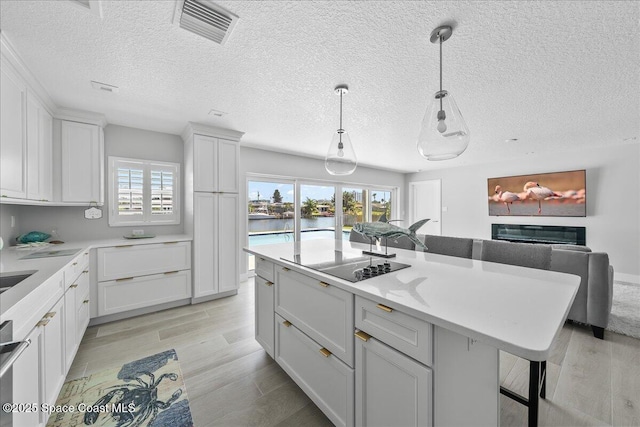 kitchen with black electric stovetop, a breakfast bar, healthy amount of natural light, decorative light fixtures, and a textured ceiling