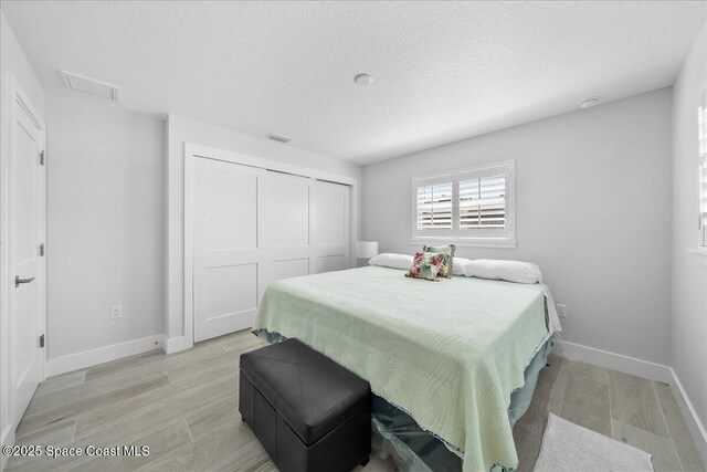 bedroom with baseboards, a textured ceiling, a closet, and light wood finished floors