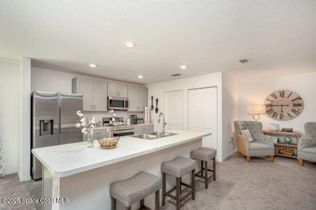 kitchen featuring stainless steel appliances, a sink, light countertops, a breakfast bar area, and a kitchen island with sink