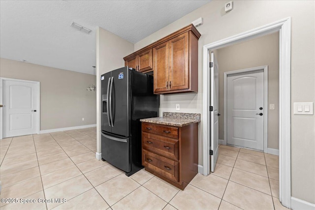 kitchen with black fridge with ice dispenser, light tile patterned floors, brown cabinetry, baseboards, and light stone counters
