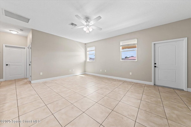 empty room with a ceiling fan, light tile patterned floors, baseboards, and a textured ceiling
