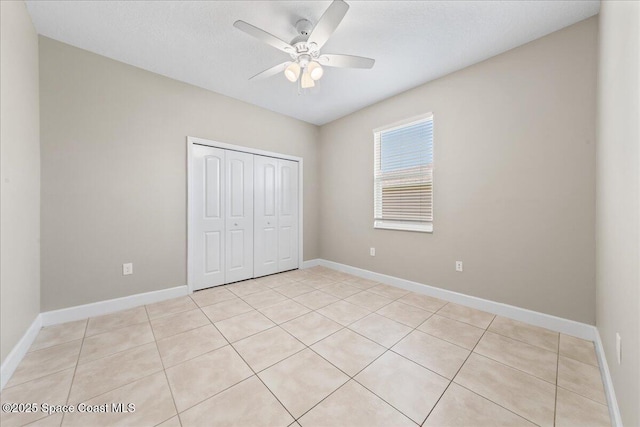 unfurnished bedroom with a closet, baseboards, light tile patterned flooring, and ceiling fan