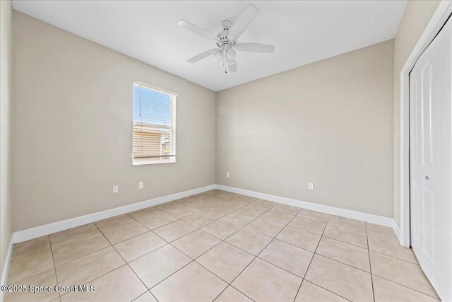 unfurnished bedroom with a closet, light tile patterned flooring, baseboards, and a ceiling fan