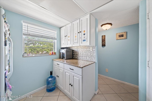 kitchen with white cabinets, light tile patterned floors, baseboards, and tasteful backsplash