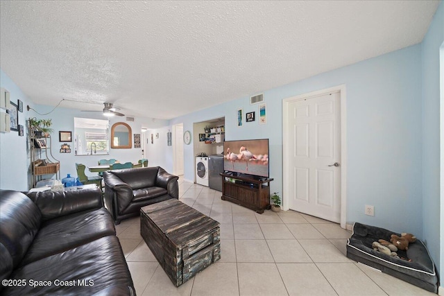 living room featuring ceiling fan, washing machine and clothes dryer, light tile patterned floors, and a textured ceiling
