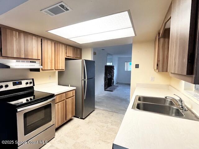 kitchen with appliances with stainless steel finishes, a sink, under cabinet range hood, and light countertops