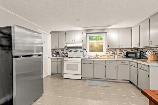 kitchen featuring freestanding refrigerator, white range with gas stovetop, under cabinet range hood, gray cabinets, and decorative backsplash
