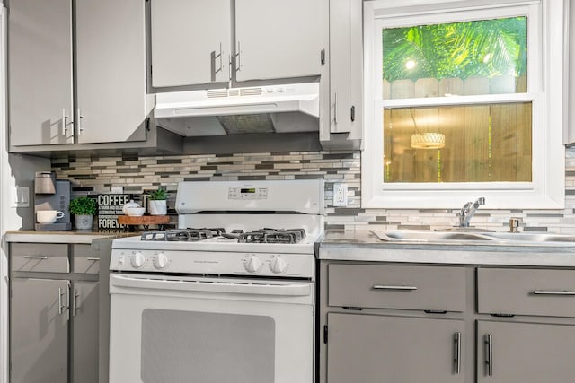 kitchen with white range with gas stovetop, under cabinet range hood, gray cabinets, a sink, and light countertops