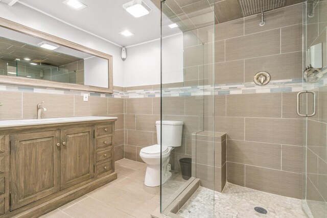 bathroom with tile walls, toilet, a stall shower, tile patterned floors, and vanity