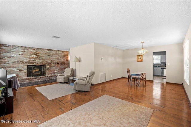 965 Bluegrass Ln, Rockledge, FL 32955 - living area with wood-type flooring, a textured ceiling, a brick fireplace, a chandelier, and baseboards