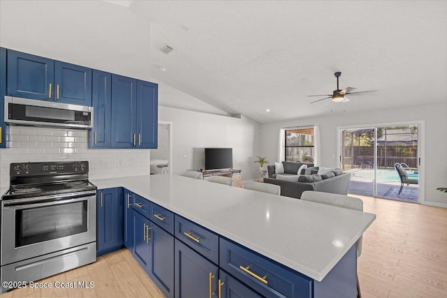 1709 Palm Ridge Rd, Melbourne, FL 32935 - kitchen featuring appliances with stainless steel finishes, a peninsula, blue cabinets, lofted ceiling, and a textured ceiling