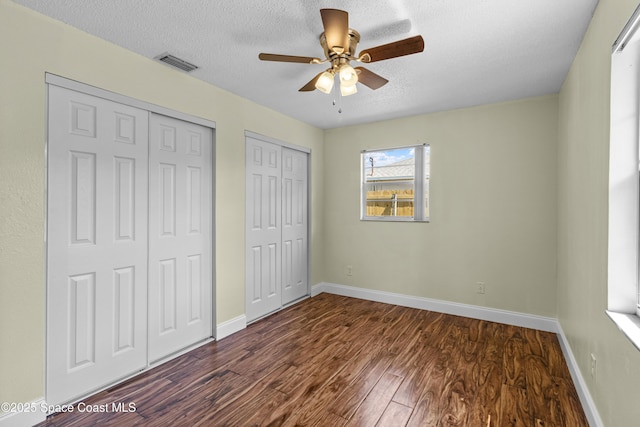 7034 Bayfront Rd, Cocoa, FL 32927 - unfurnished bedroom featuring two closets, dark wood-type flooring, baseboards, a textured ceiling, and a ceiling fan