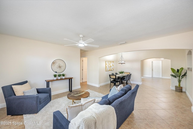 living area with arched walkways, a ceiling fan, light tile patterned flooring, and baseboards