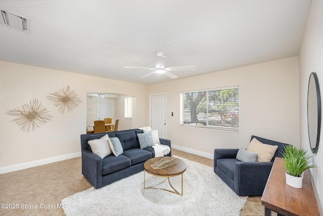 living room featuring ceiling fan, baseboards, arched walkways, and light tile patterned flooring