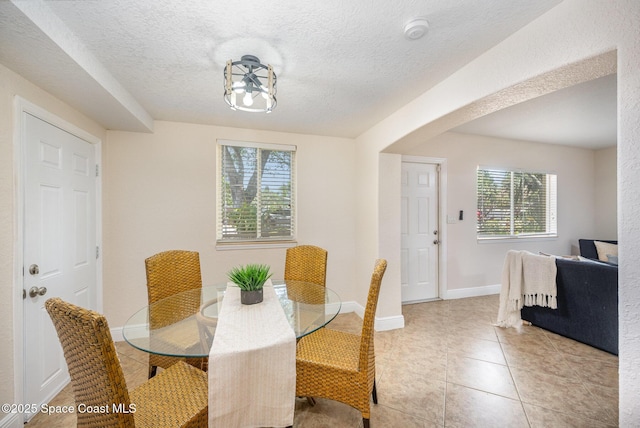 dining space featuring light tile patterned floors, a textured ceiling, and baseboards