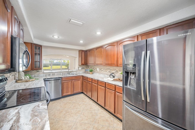 kitchen featuring stainless steel appliances, a sink, arched walkways, backsplash, and a textured ceiling