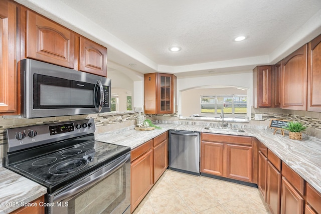 kitchen with appliances with stainless steel finishes, a sink, tasteful backsplash, brown cabinets, and a textured ceiling