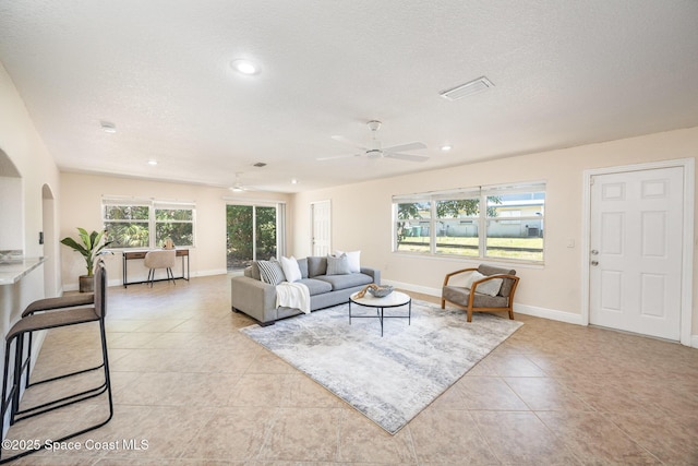 living area featuring arched walkways, a ceiling fan, light tile patterned flooring, recessed lighting, and a textured ceiling