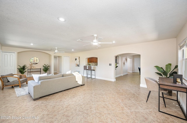 living room featuring arched walkways, ceiling fan, recessed lighting, a textured ceiling, and baseboards